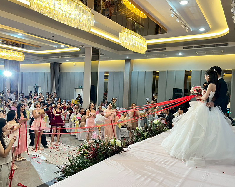 Guests holding red ribbons during a wedding ceremony under crystal chandeliers